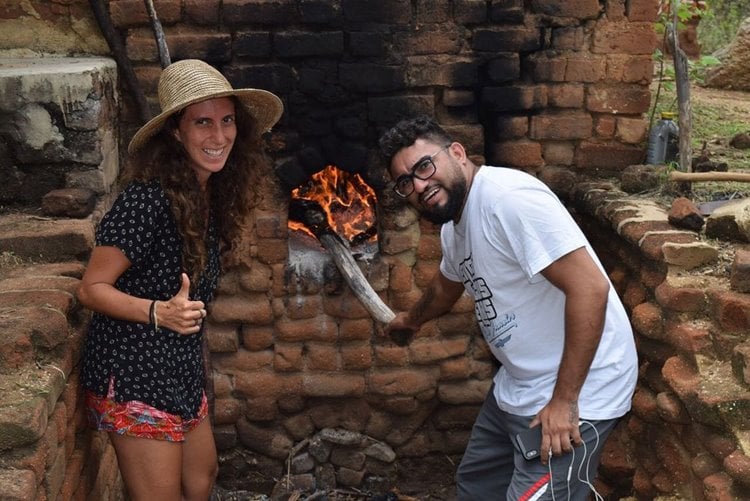 Influenciadora  Júlia Tolezano ao lado de homem em um tipo de forno rústico