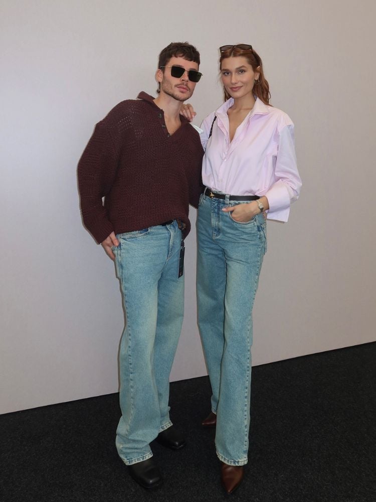 João Figueiredo usando tricô marrom e calça jeans e Sasha usando camisa rosa e calça jeans 