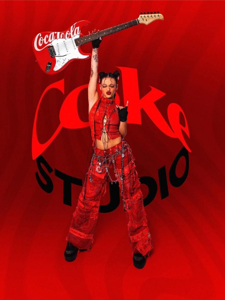 Clara Garcia usando cropped e calça vermelhos, segurando guitarra em vermelho e branco, com "coke studio" escrito atrás