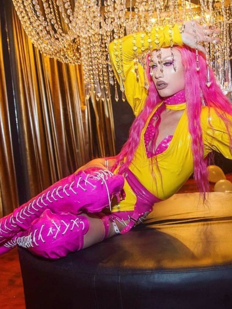 Drag queen usando cabelo rosa, body amarelo e botas longas rosas 