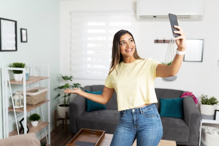 Mulher de pele clara usando blusa amarela e calça jeans gravando um ambiente com o celular