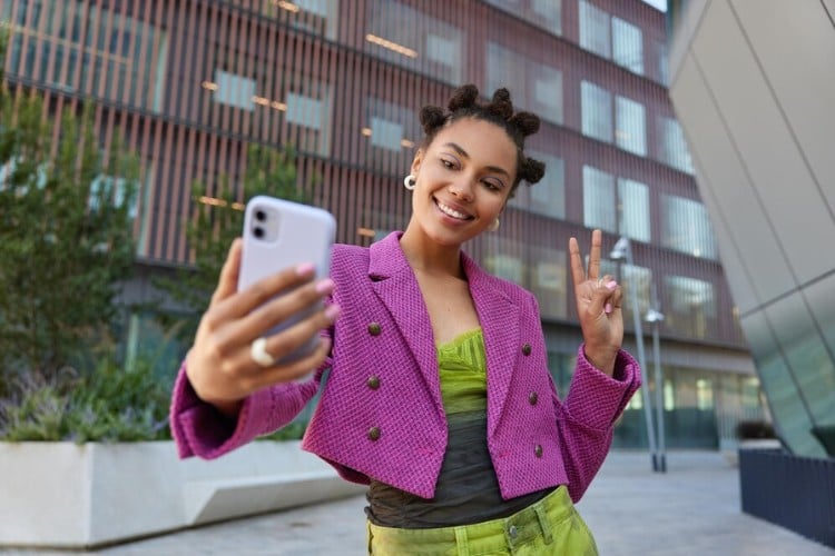 Mulher de pele negra usando roupa verde e roxa, tirando selfie 