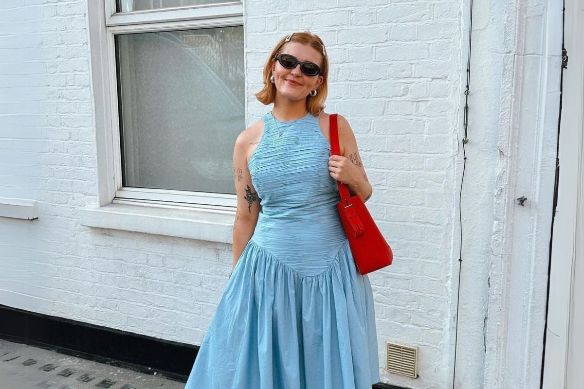 Foto de mulher de cabelos loiros curtos usando óculos de sol vintage, bolsa vermelho e vestido de verão azul claro