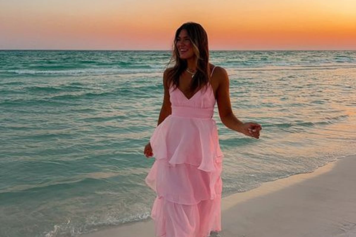 Foto de mulher loira na praia usando vestido longo de babados rosa claro