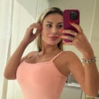 Selfie da influencer Andressa Urach em frente ao espelho usando macaquinho rosa e segurando celular com capinha roxa