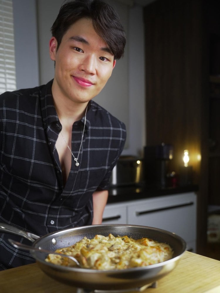 Arthur Paek usando camisa zadrez azul-marinho e cozinhando em frigideira 