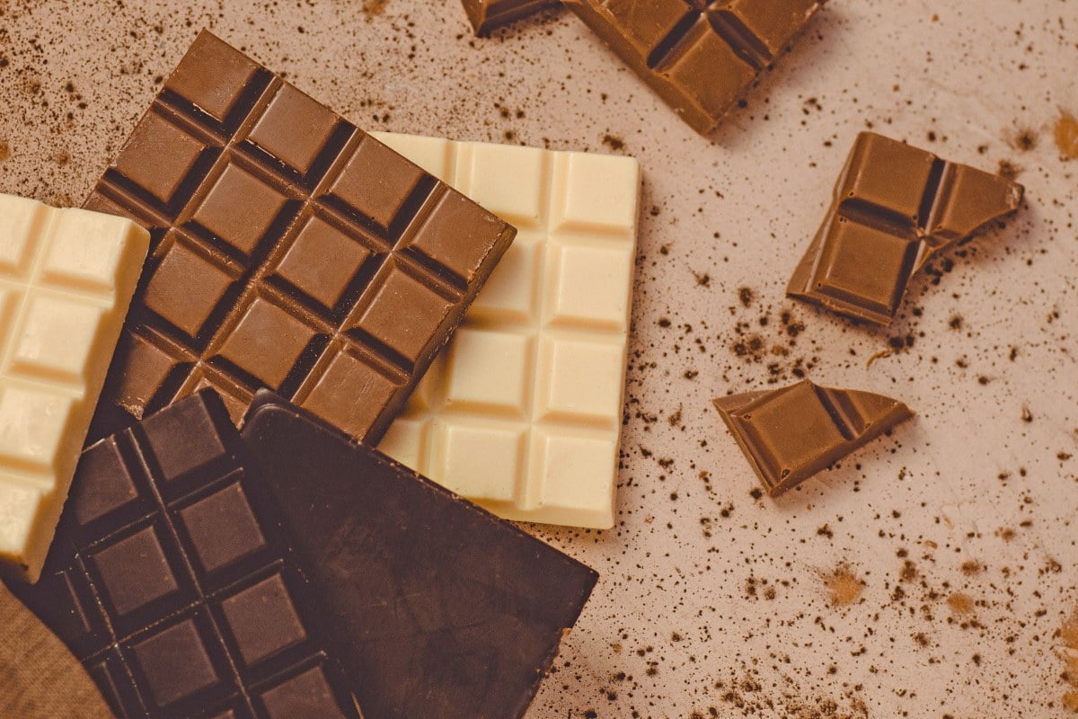 Foto de mesa com barras e pedaços de chocolate ao leite, amargo e branco