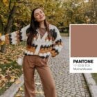 A imagem mostra uma mulher em um parque outonal, vestindo um cardigã de tricô em tons terrosos e calças marrons. Ela sorri segurando folhas amarelas. Ao lado, a cor "Mocha Mousse" da Pantone é exibida.