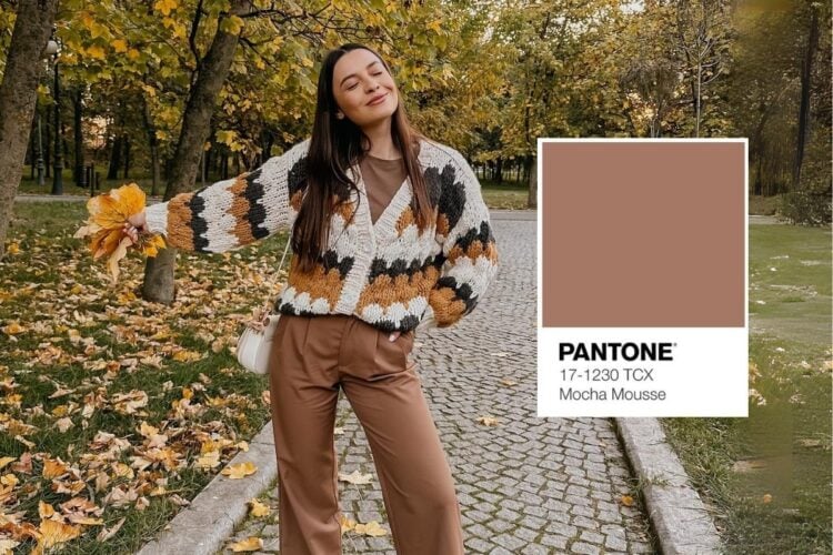 A imagem mostra uma mulher em um parque outonal, vestindo um cardigã de tricô em tons terrosos e calças marrons. Ela sorri segurando folhas amarelas. Ao lado, a cor "Mocha Mousse" da Pantone é exibida.