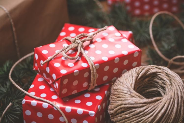 Presentes festivos embrulhados em papel vermelho com estampa de bolinhas brancas, adornados com corda de sisal. Ao lado, um rolo de barbante adiciona um toque rústico, enquanto galhos de pinheiro completam a decoração, criando uma cena natalina acolhedora e encantadora.