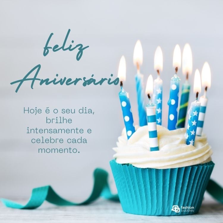 A imagem apresenta um cupcake com cobertura branca e velas azuis acesas, decoradas com listras e estrelas. Ao lado, está a mensagem: "Feliz Aniversário. Hoje é o seu dia, brilhe intensamente e celebre cada momento." O fundo é claro.