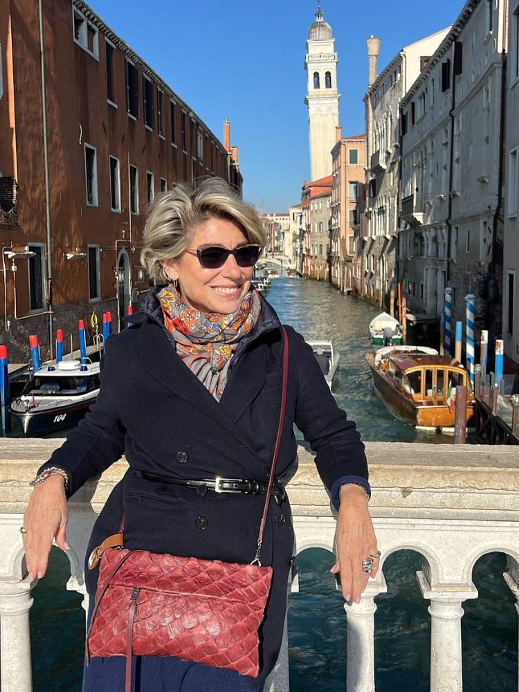 Consuelo Blocker usando roupa preta, bolsa vermelha e canal de Veneza ao fundo