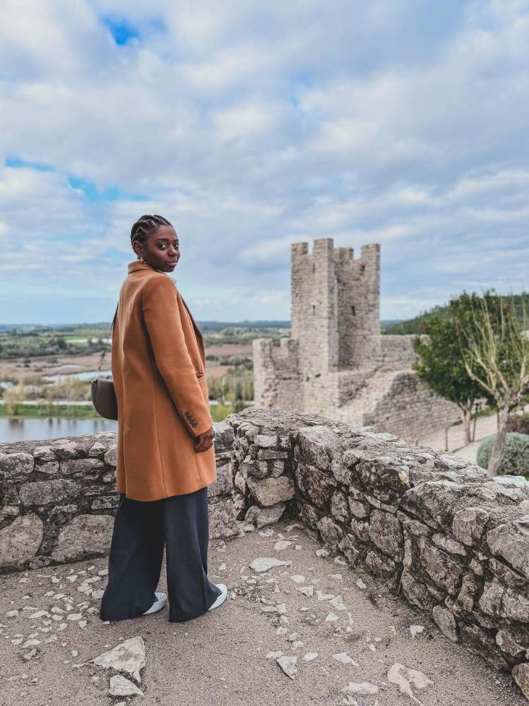 Jacira usando sobretudo marrom e calça preta próxima ao Castelo de Montemor o Velho