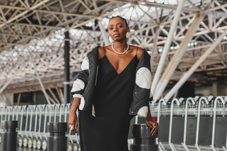 Jacira Doce no aeroporto de Brasília usando slipdress preto, casaco branco e preto