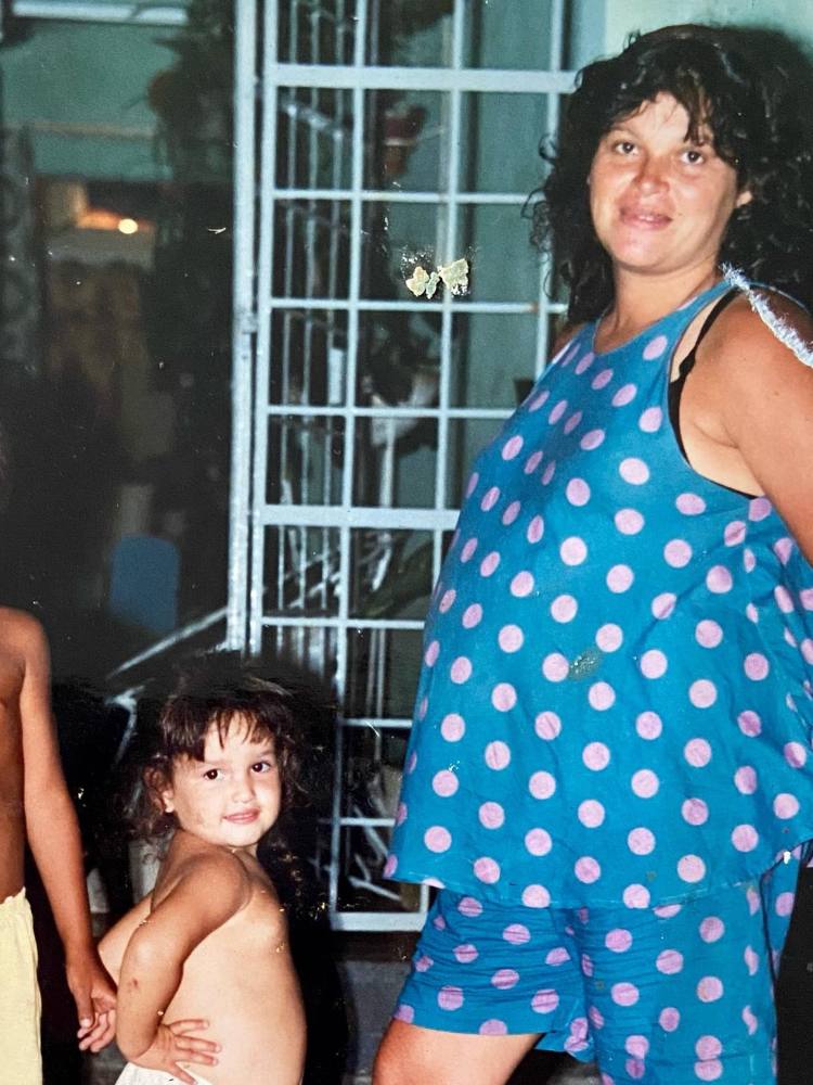 Foto antiga de Juliette criança ao lado de sua mãe que usa conjunto azul de bolas rosas