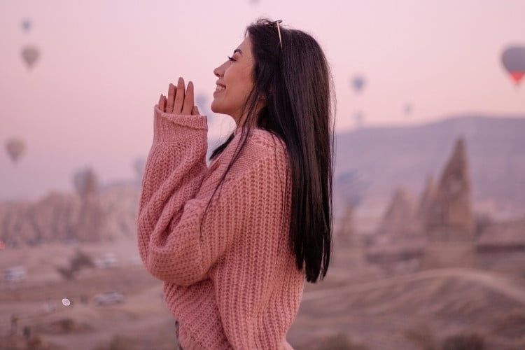 Foto de mulher morena usando suéter de lã rosa e com as mãos em oração