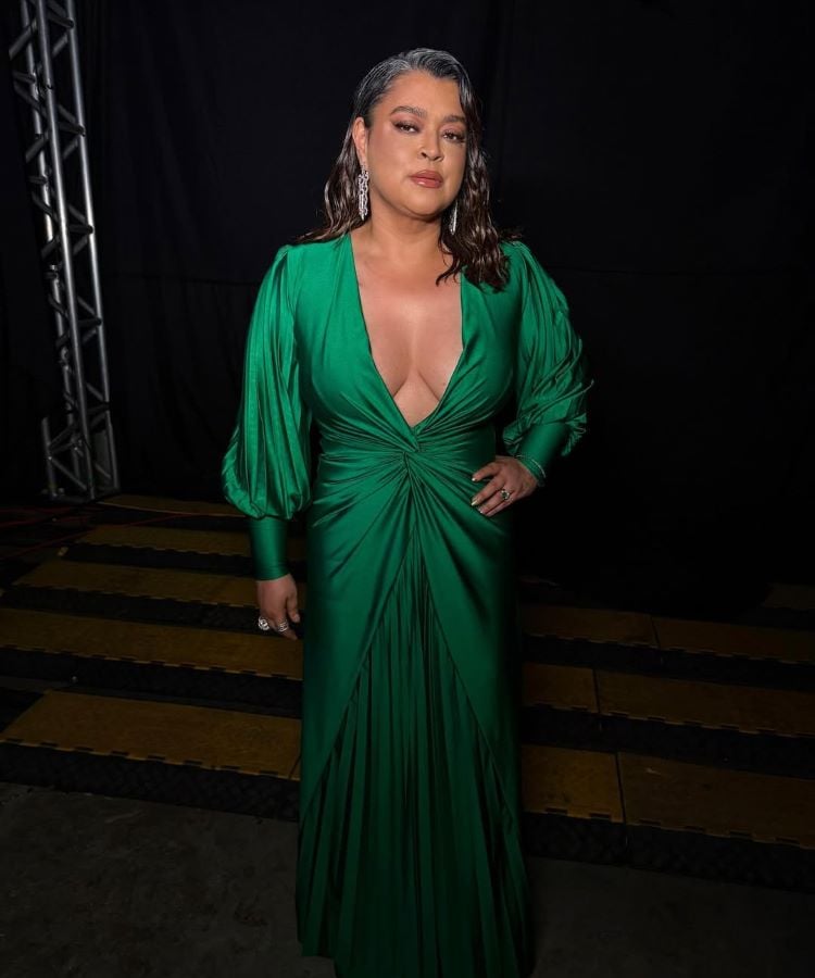 Preta Gil em vestido verde esmeralda com decote profundo e mangas volumosas, para o Prêmio Multishow 2024 looks. Cabelo solto e ondulado, maquiagem suave, brincos longos. Fundo escuro com iluminação destacando a figura elegante.