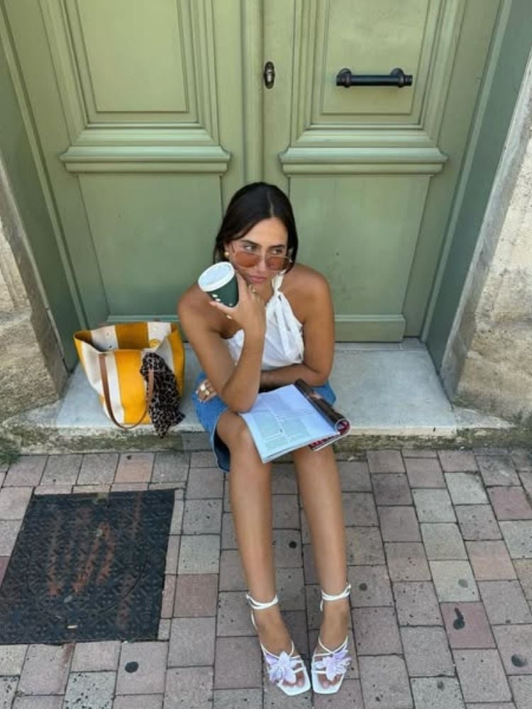 Mulher usando camiseta branca, bermuda jeans e sapato branco com aplicação de flor