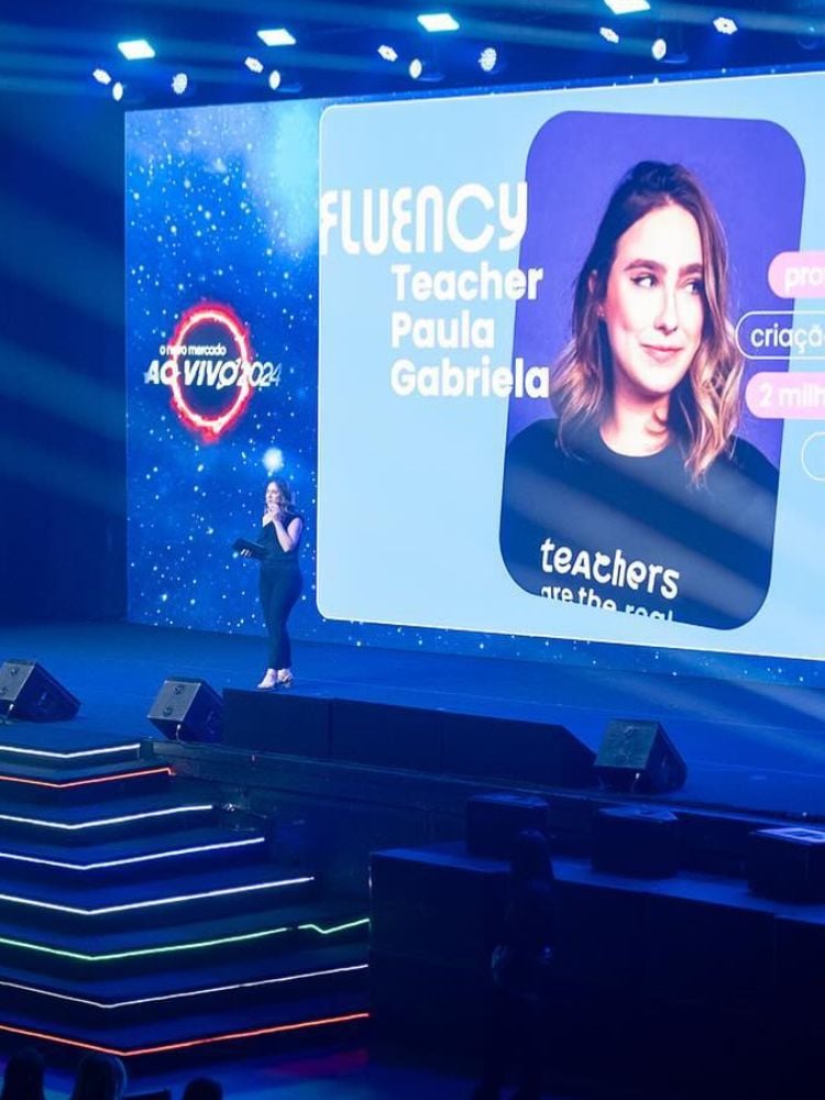 Paula Gabriela de look all black palestrando no palco do RD Summit com foto da influencer no telão ao fundo