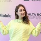 Teacher Paula Gabriela usando suéter amarelo em frente a painel do YouTube