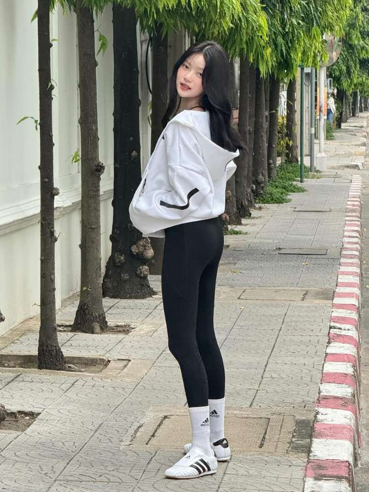 Mulher de origem asiática na calçada usando moletom branco, legging preta e Adidas Taekwondo branco e preto