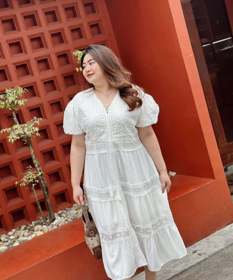 Mulher com vestido soltinho branco, bolsa, fundo terracota de loja.