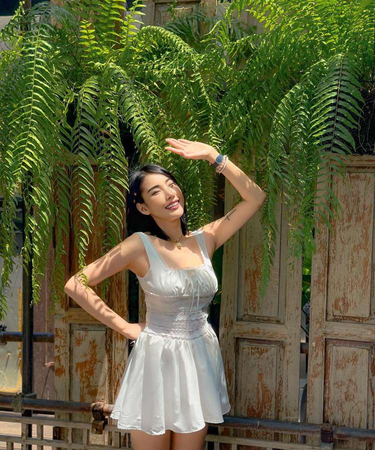 Mulher com vestido corset branco, fundo de madeira, samambaias acima.