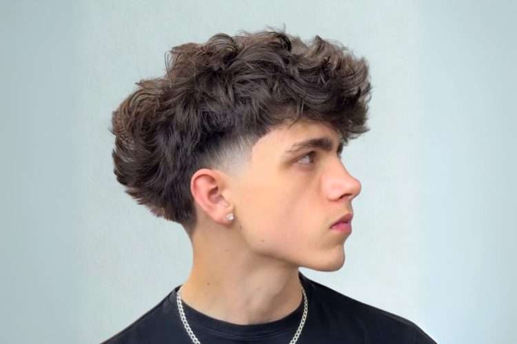 Um homem jovem, de perfil, com um corte de cabelo moderno. Ele tem um **low fade** nas laterais e na nuca, e o topo do cabelo é mais longo, com volume e textura cacheada.