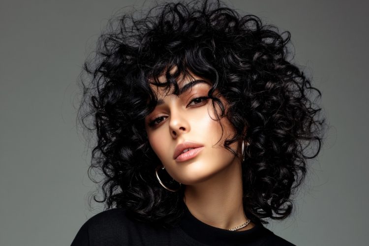 Foto de mulher de cabelo enrolado médio usando blusa preta em fundo cinza